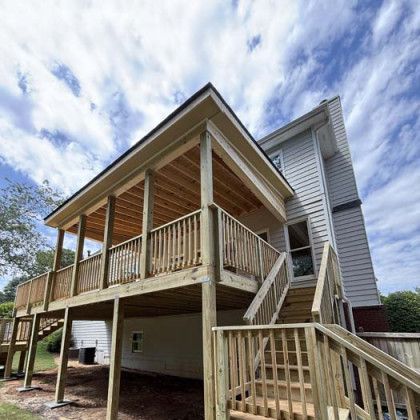 Elevated house with wooden porch, stairs, and railing under a partly cloudy sky