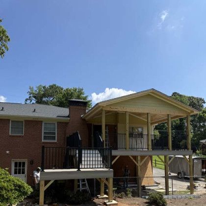 Brick house with a raised porch, black railings, and a large covered deck under a blue sky