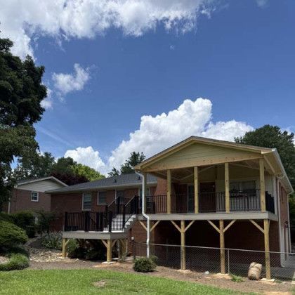 House with a raised wooden porch and brick lower level under a blue sky with clouds