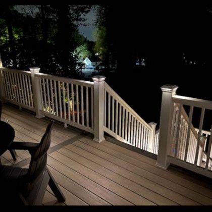 Nighttime wooden deck with white railing, stairs, and a table and chair in the foreground