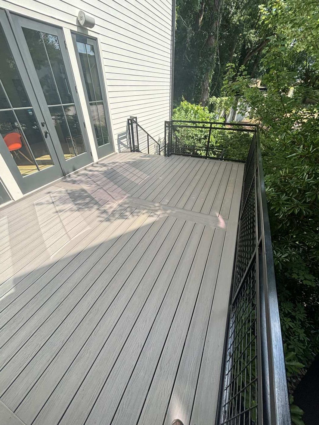 Wooden deck beside a house, with glass doors, railing, and trees below.