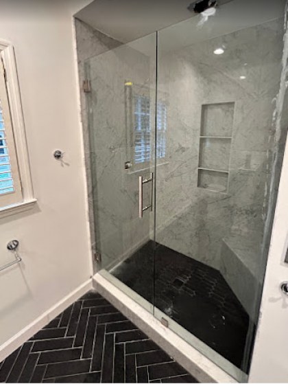 Glass walk-in shower with black herringbone floor tile and white marble walls and shelves
