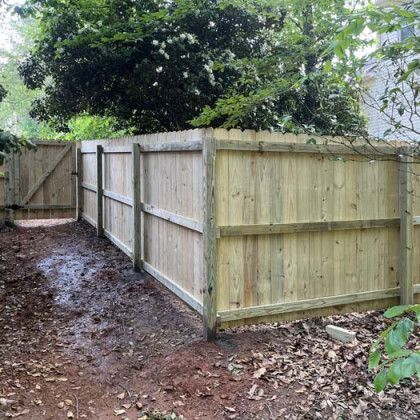 Freshly built wooden fence and gate bordering a muddy backyard path under trees