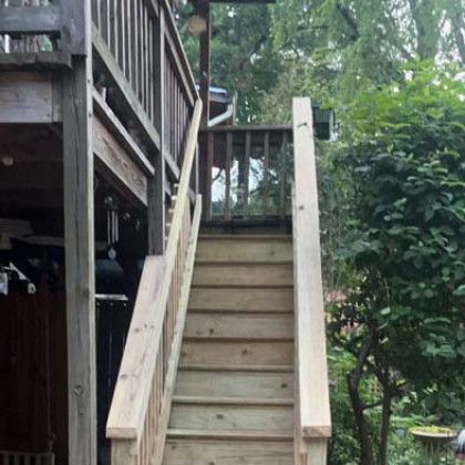 Wooden outdoor staircase leading to a raised deck beside trees and greenery