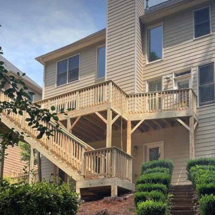 Multi-level beige house with exterior wooden staircases and balconies, viewed from the yard