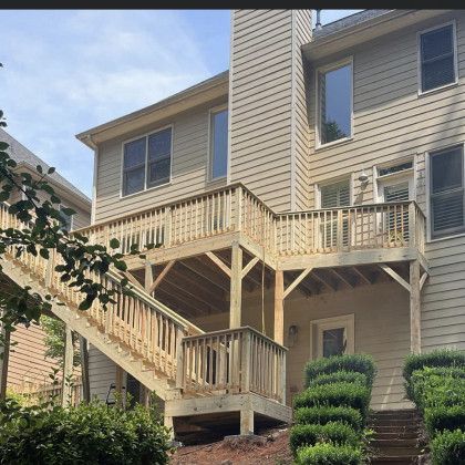 Exterior of a tan house with an elevated wooden deck and staircase in front of landscaped shrubs