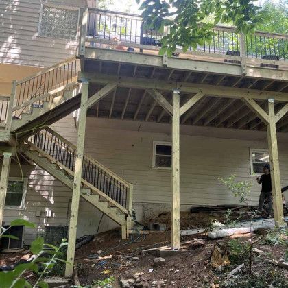 Wooden deck and staircase on a house with support posts over a sloped, wooded yard