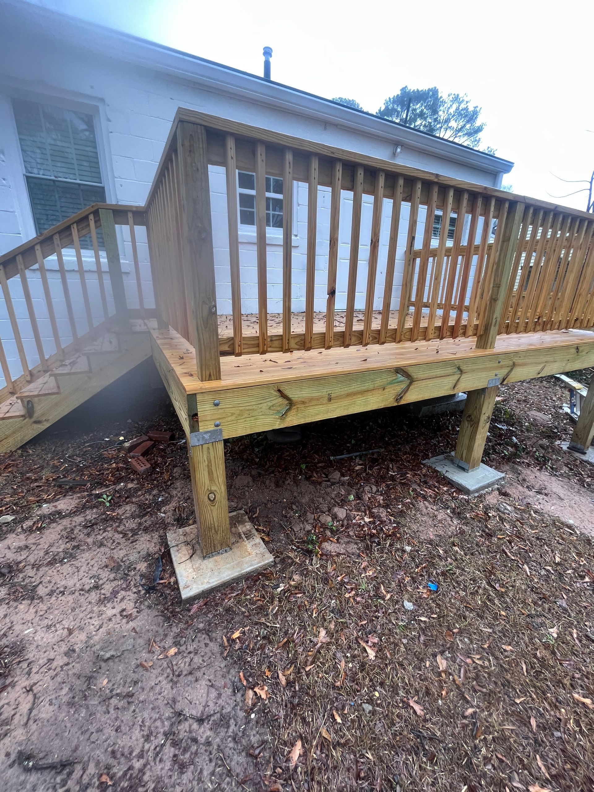 Wooden deck ramp with railings beside a house, supported by posts over gravel.