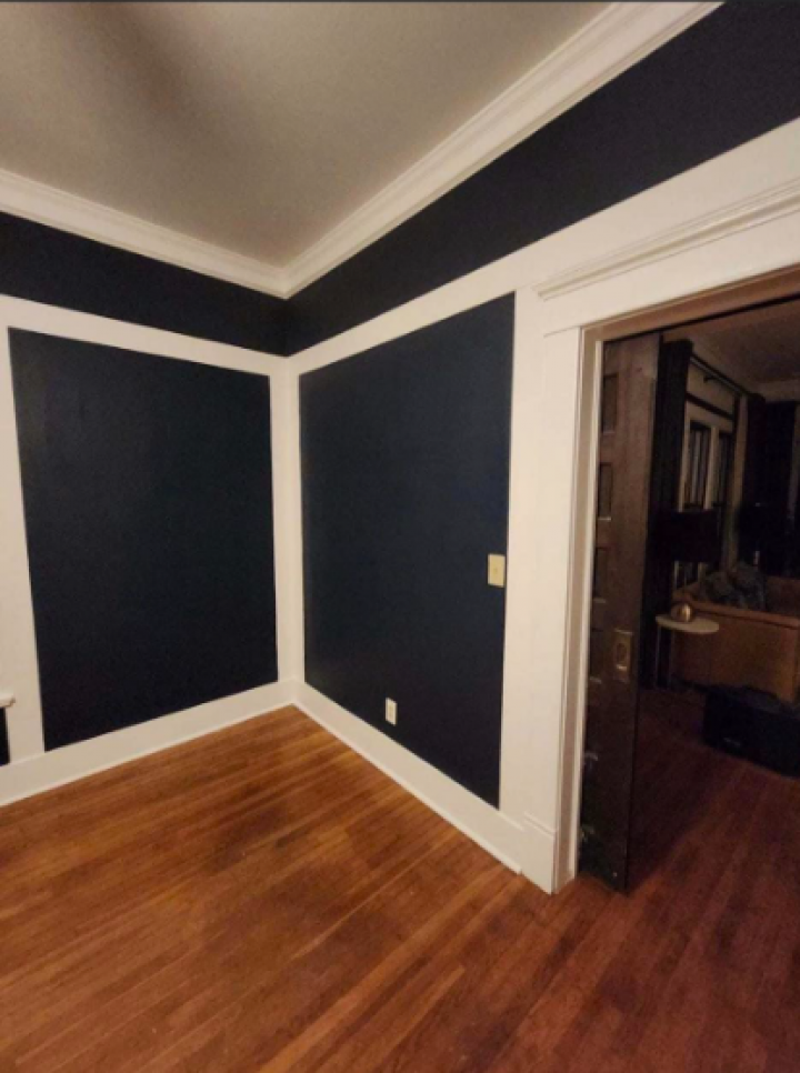 Empty room with dark blue accent walls, white trim, wood floor, and an open doorway.