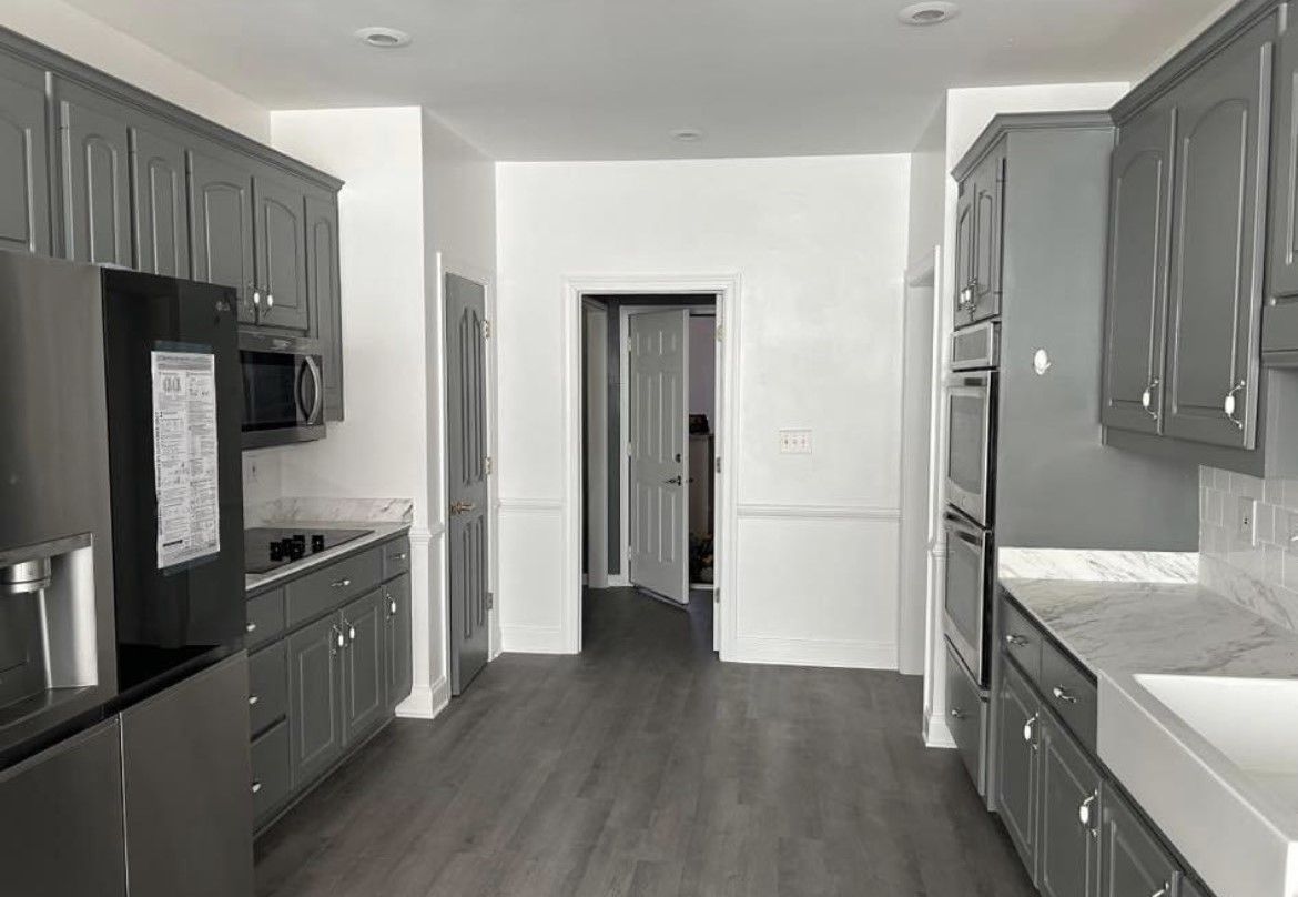 Modern kitchen with gray cabinets, dark wood floors, and stainless steel appliances, seen from the center aisle