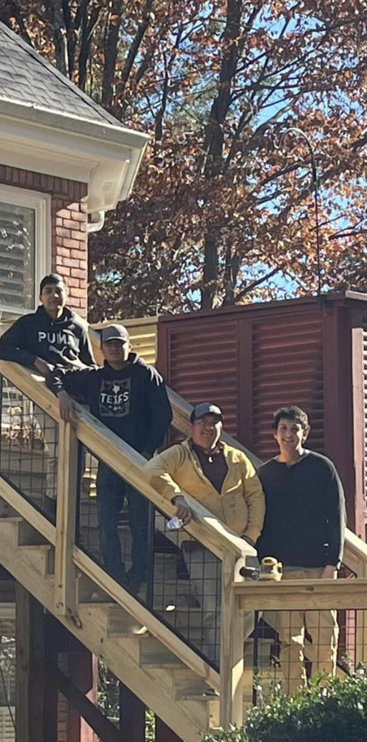 Four people on a wooden staircase outside a house, with autumn trees in the background.