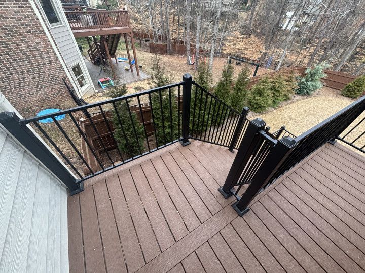 Wooden deck with black railing overlooking a wooded backyard and stairs leading down to the yard
