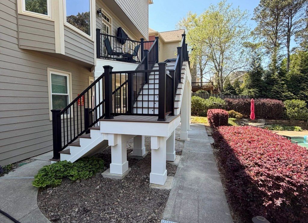 Outdoor apartment stairway with black railings and white support posts beside a landscaped path