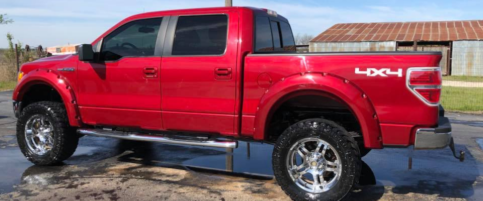 Red lifted pickup truck parked outdoors, side view, with chrome wheels and 4x4 decal