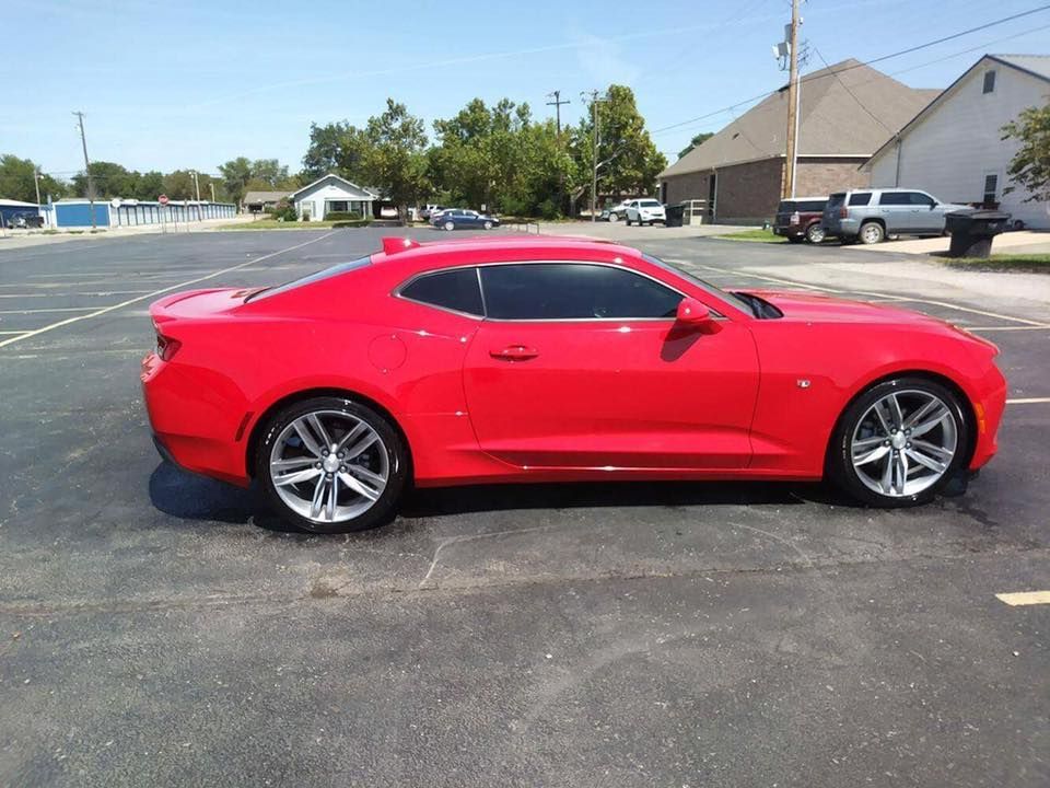 Red sports coupe parked on an asphalt lot under a clear sky.