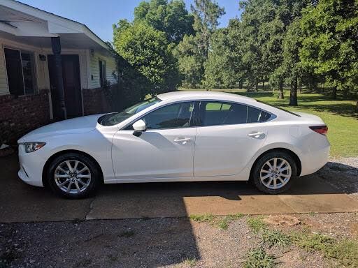 White sedan parked in a driveway beside a house on a sunny day