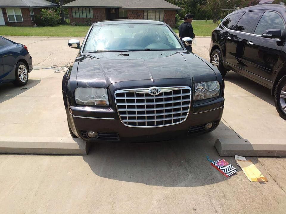 Brown Chrysler sedan parked in a driveway between two cars, with a person standing nearby