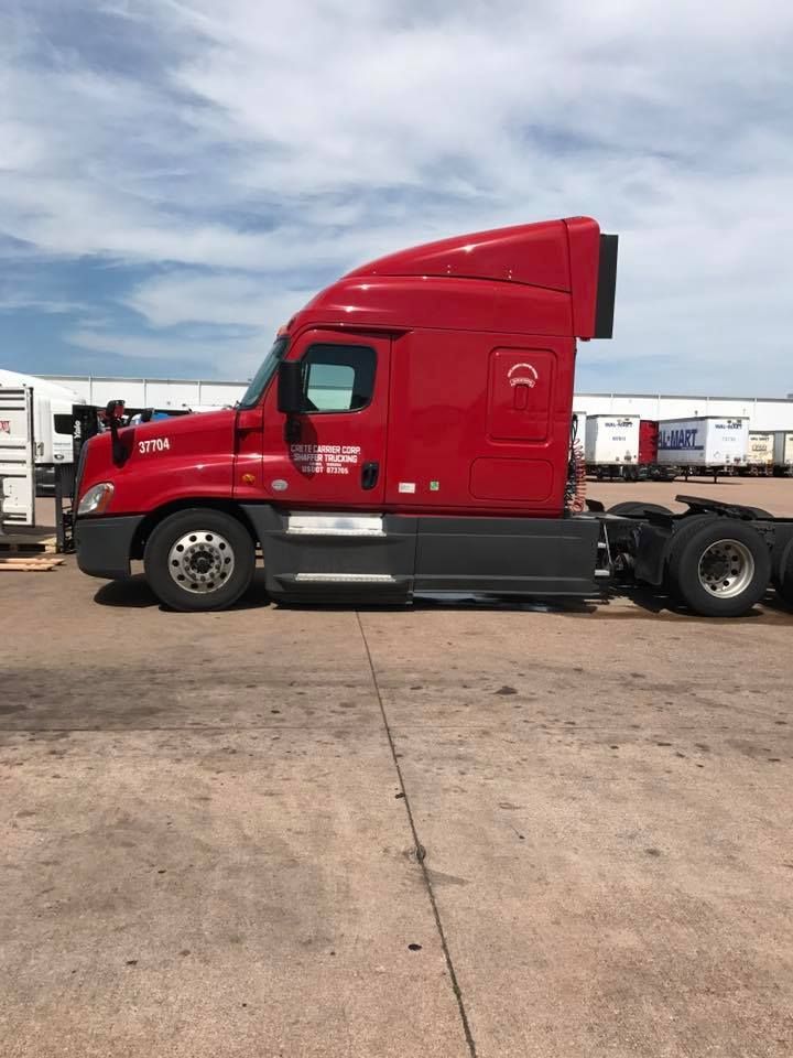 Red semi-truck cab parked in an open lot under a cloudy sky.