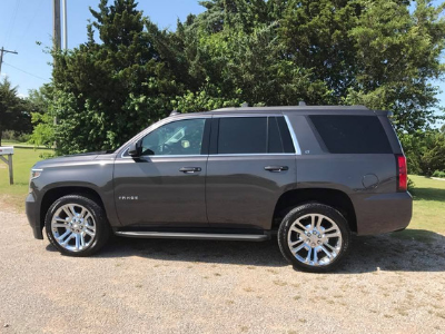 Dark gray SUV parked on a gravel driveway beside green trees on a sunny day