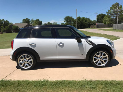 Silver Mini Cooper parked on a driveway under a sunny sky.