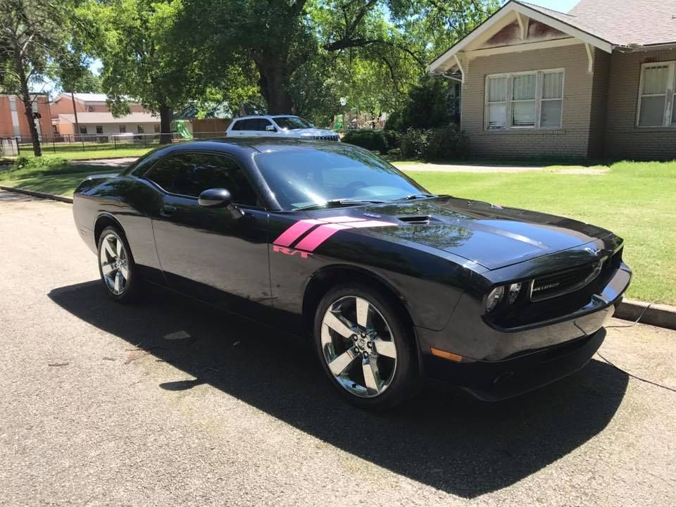 Black sports car with pink stripes parked on a sunny residential street