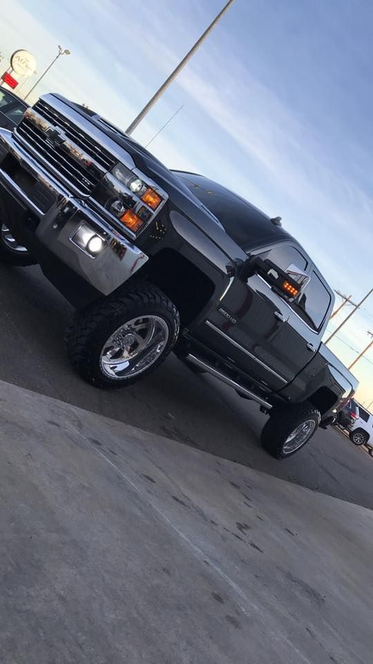 Black lifted pickup truck angled in a parking lot under a blue sky