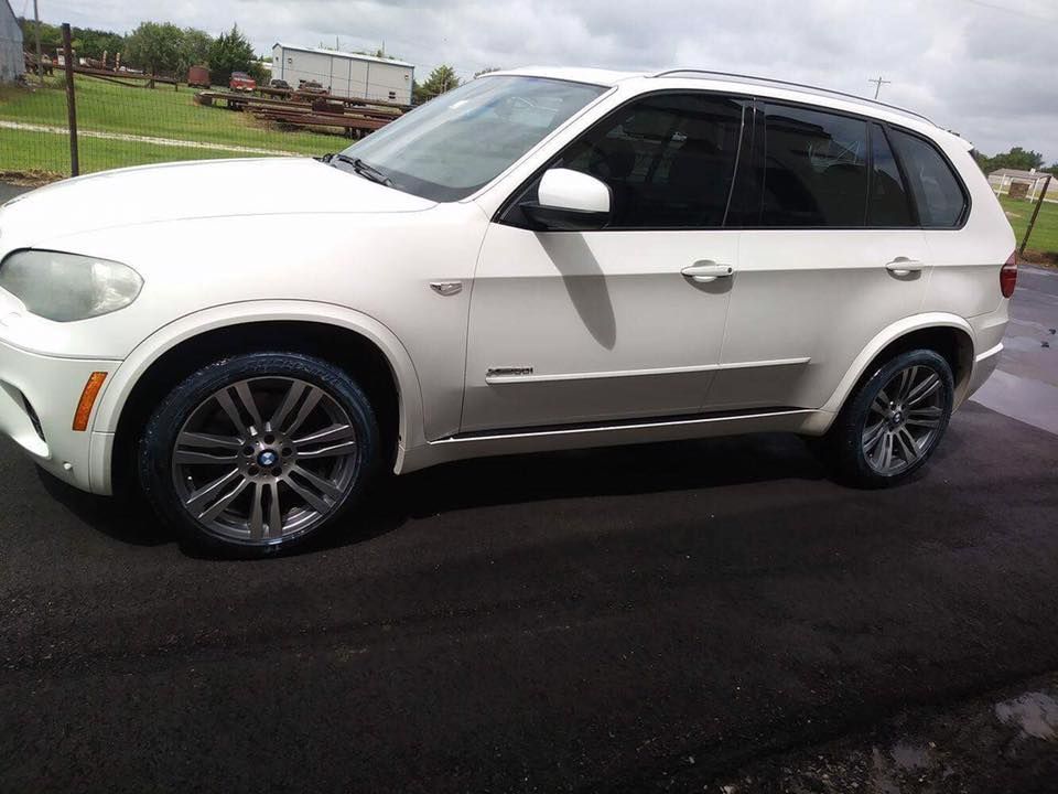 White SUV parked on a paved lot beside a grassy roadside, viewed from the front-left side.