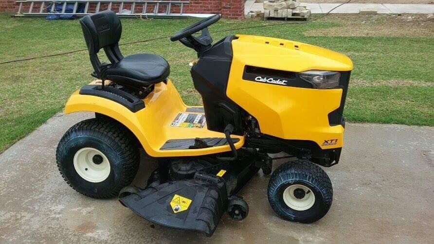 Yellow riding lawn mower parked on a driveway beside a grassy lawn