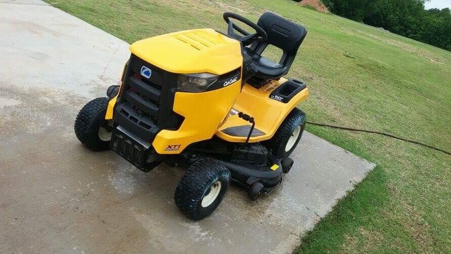 Yellow riding lawn mower parked on a wet driveway beside grass