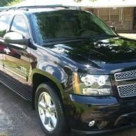 Black SUV parked in a driveway, angled front view, with chrome grille and shiny wheels