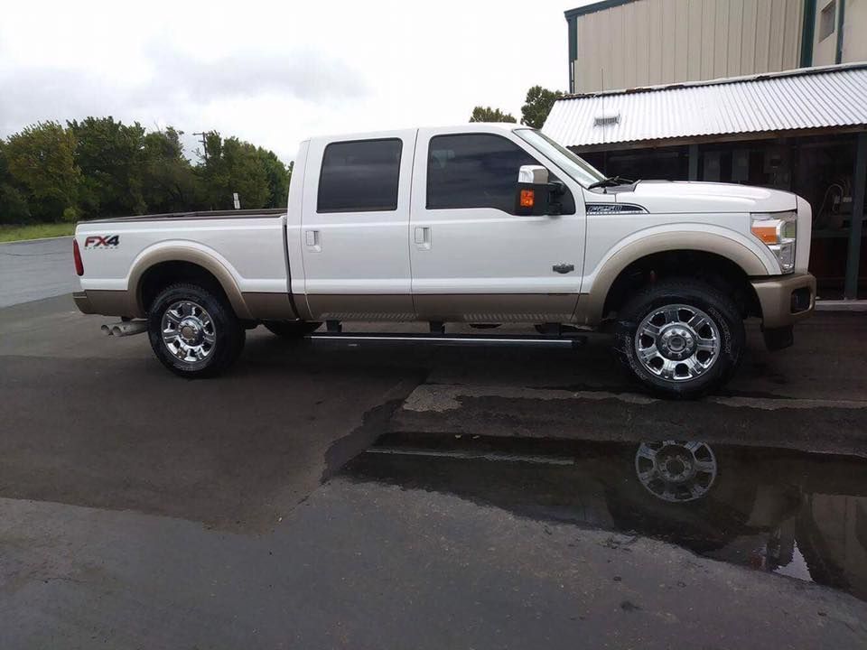 White pickup truck parked on wet pavement beside a building, reflected in a puddle