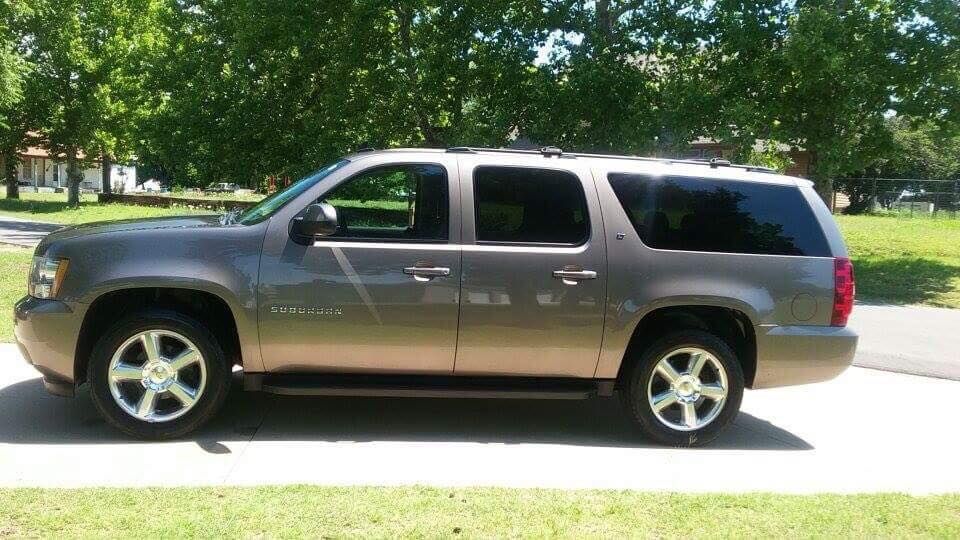 Gray SUV parked on a sunny suburban street beside a grassy lawn and trees