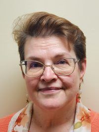 Head-and-shoulders portrait of a smiling person with glasses against a plain beige background.