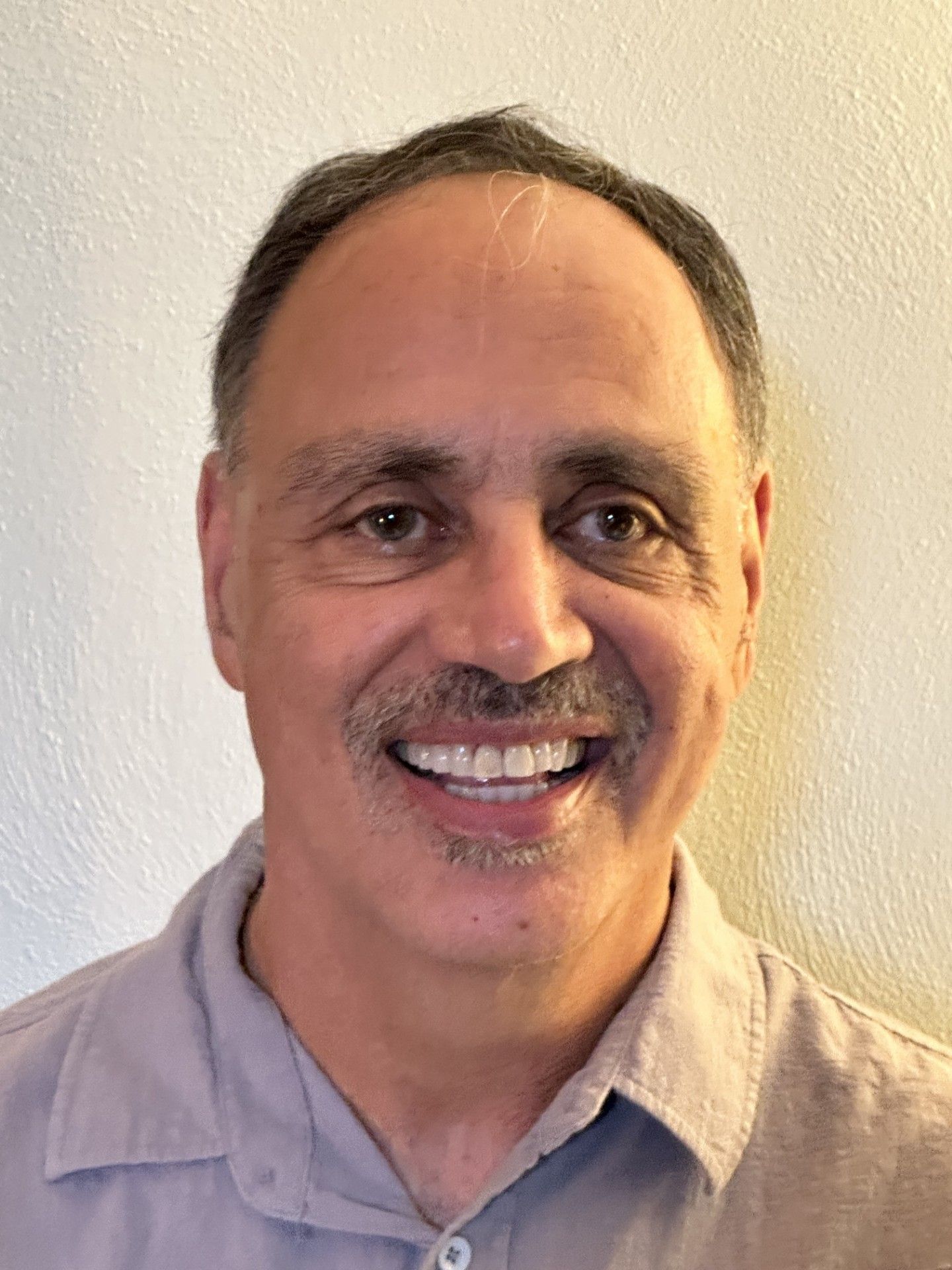 Smiling man in a light gray shirt against a plain beige wall