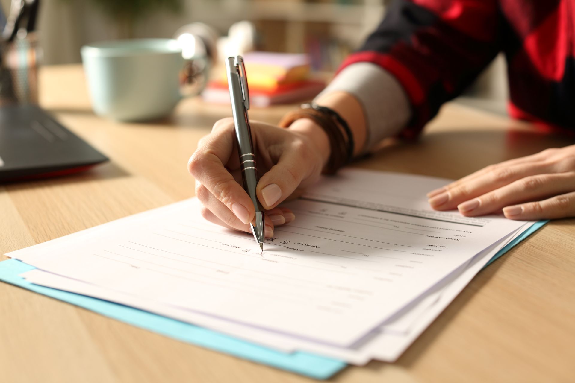 Hand writing on a checklist at a desk with a laptop and mug nearby