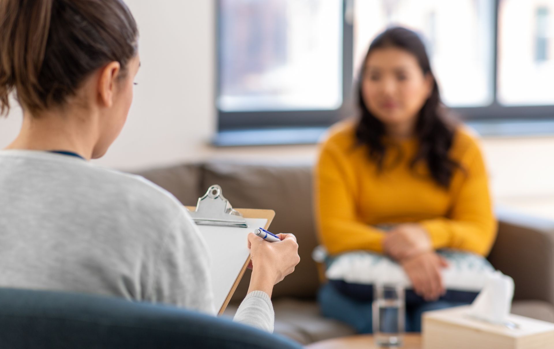 Therapist taking notes while client sits on a couch in a counseling office