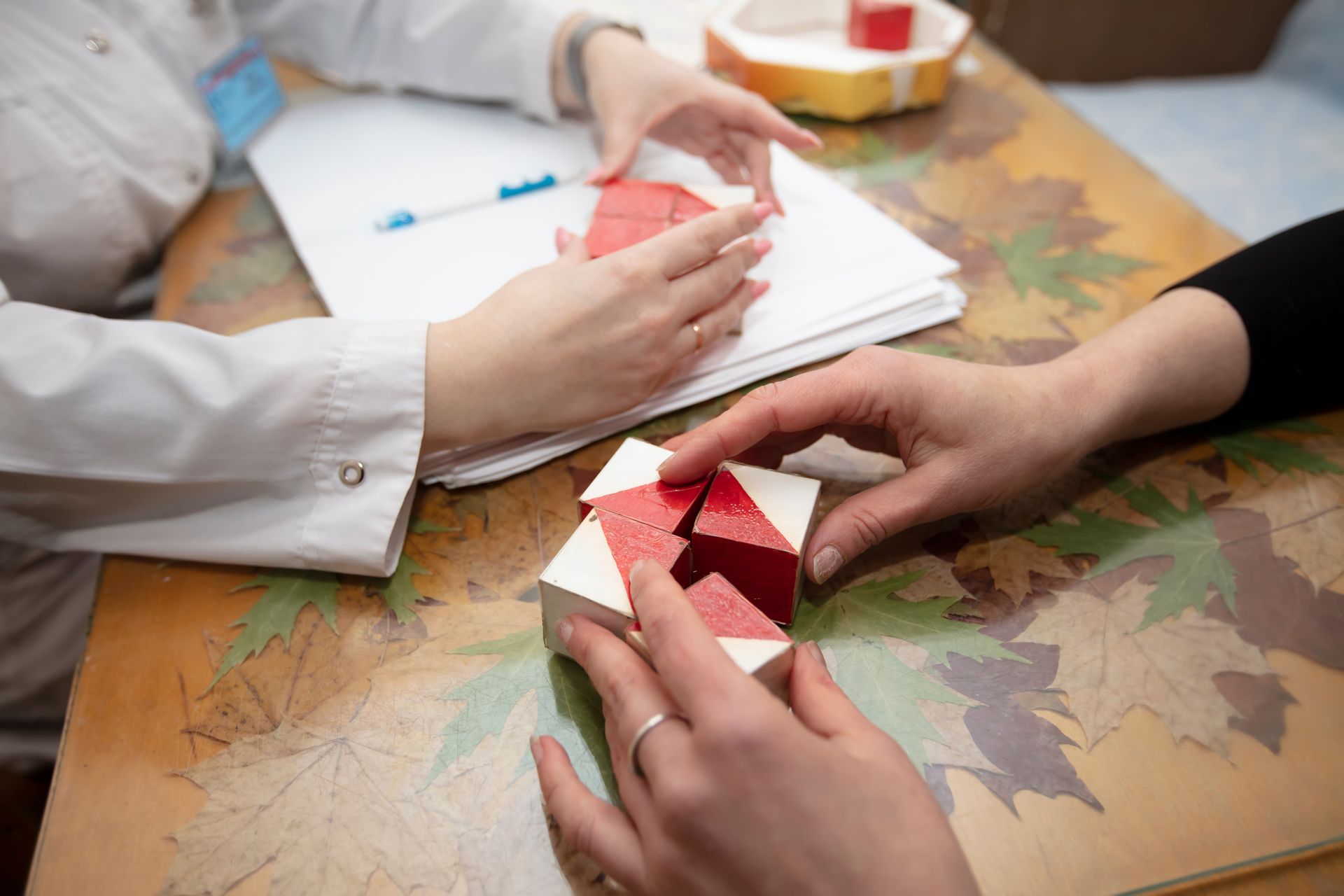 Hands folding red paper origami at a table with autumn leaf decorations