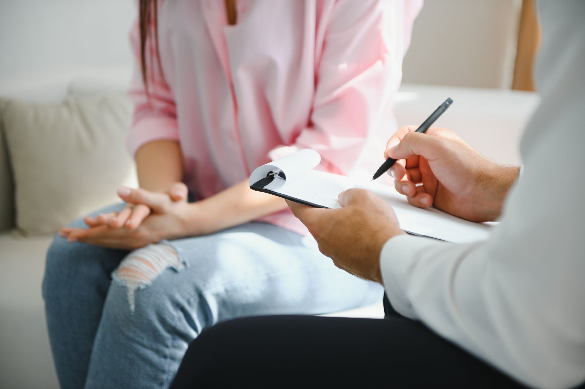 Therapist taking notes while speaking with a seated patient in a bright 상담 room