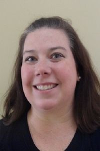 Smiling woman with shoulder-length brown hair against a plain beige background