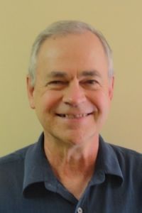 Smiling man in a dark shirt against a plain beige background