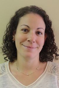 Smiling person with curly dark hair wearing a white top against a beige background