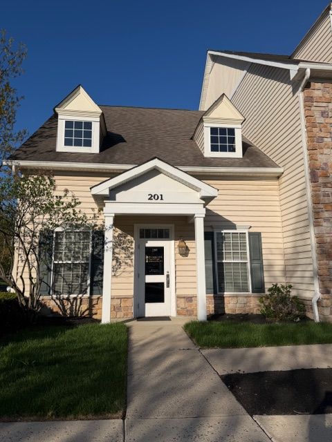 Small beige townhouse with white trim, front door marked 201, and a concrete walkway under a blue sky.