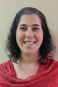 Smiling person with dark curly hair wearing a red top against a plain beige background