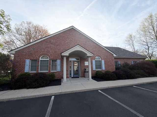Brick building with arched entrance, blue shutters, and a parking lot in front