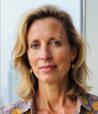 Close-up portrait of a woman with blonde hair, wearing a patterned blouse and earrings, against a soft background
