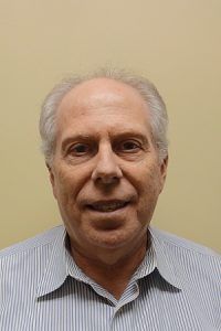 Portrait of a smiling man in a striped shirt against a plain beige background