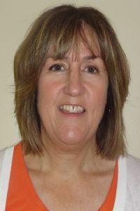 Portrait of a smiling person with shoulder-length brown hair, wearing an orange and white top on a plain background