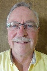Smiling man with glasses and a mustache in a light yellow shirt against a brown background