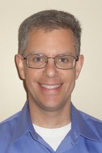 Portrait of a smiling person wearing glasses and a blue collared shirt against a plain background