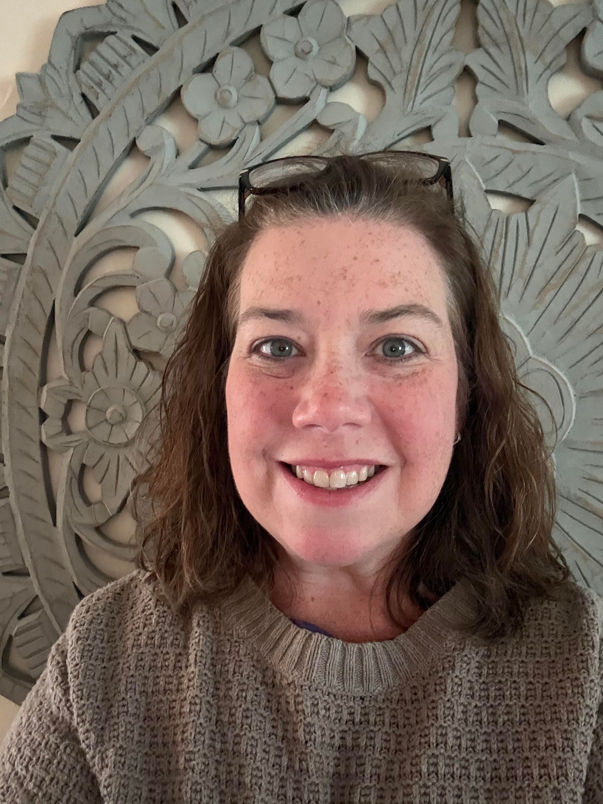 Smiling woman with shoulder-length brown hair against a plain beige background
